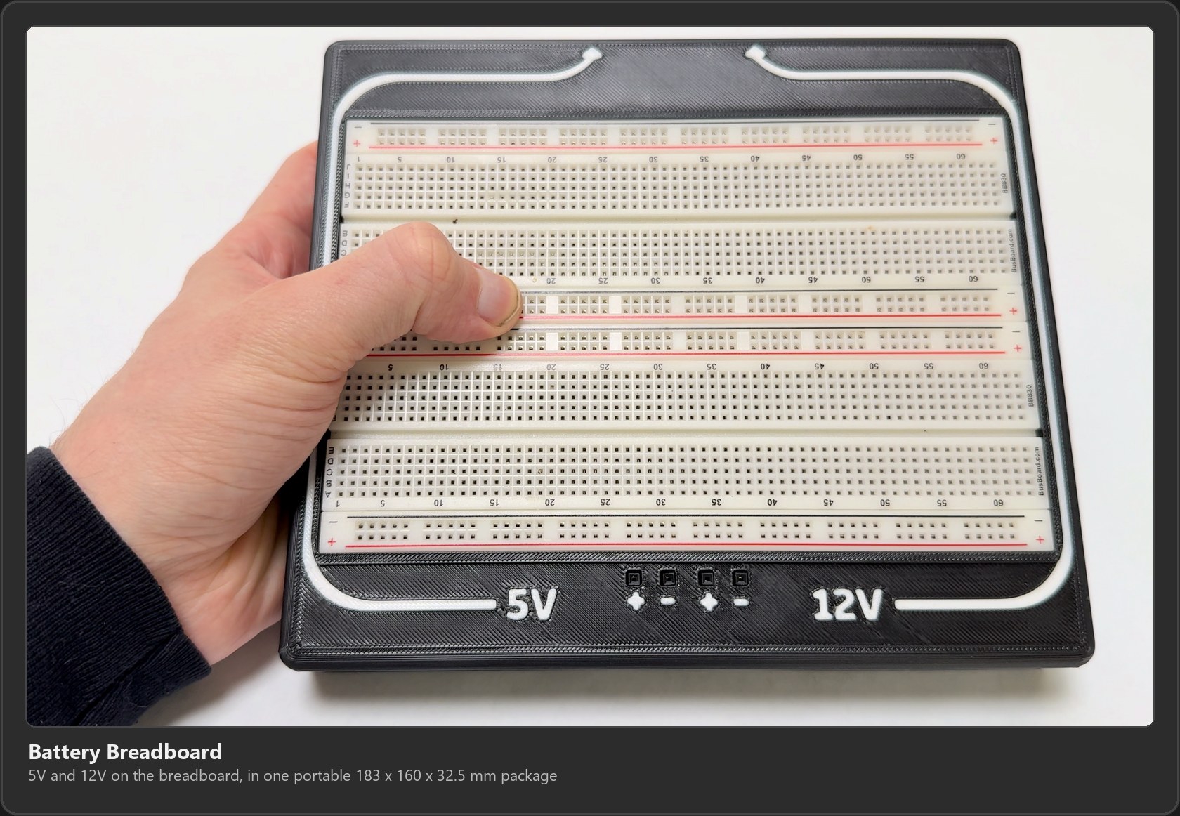 The finished Battery Breadboard held in one hand: a full-size breadboard in a black 3D printed case, with 5V and 12V labels and plus and minus Dupont sockets along the front edge