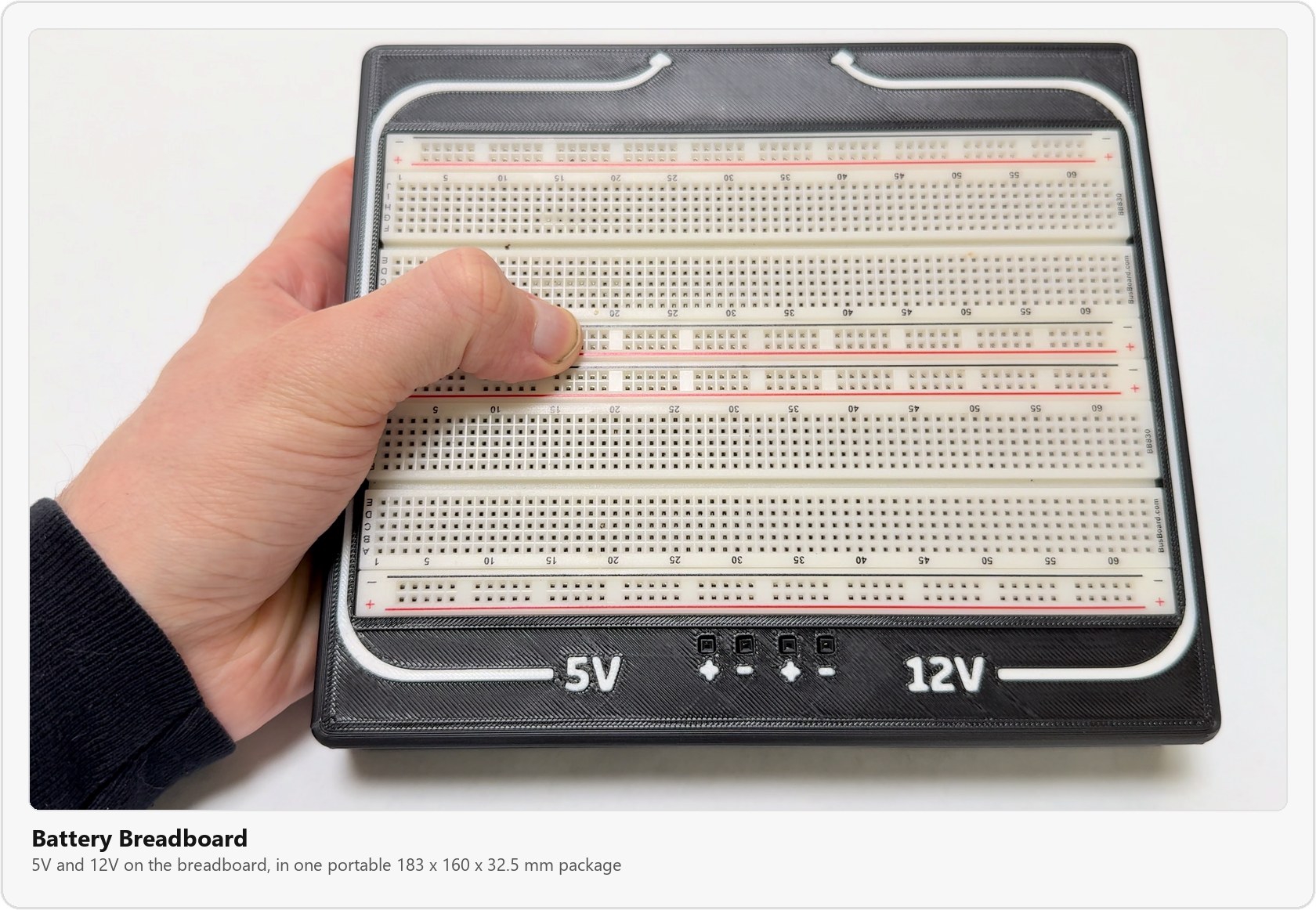 The finished Battery Breadboard held in one hand: a full-size breadboard in a black 3D printed case, with 5V and 12V labels and plus and minus Dupont sockets along the front edge