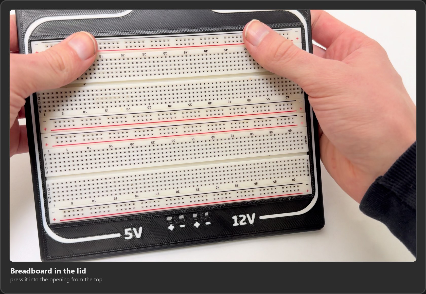 Pressing the breadboard into the lid, with the 5V and 12V labels and the plus and minus marks along the front edge