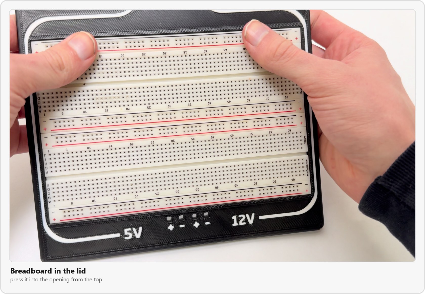 Pressing the breadboard into the lid, with the 5V and 12V labels and the plus and minus marks along the front edge